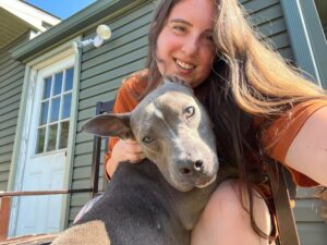 A woman holding a dog in front of a house.